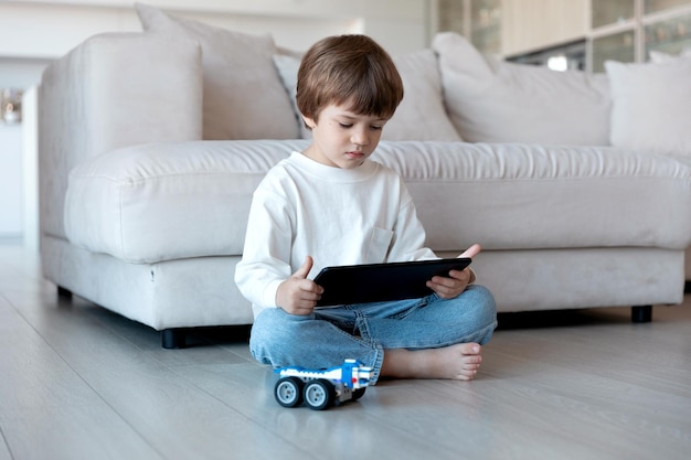 Niño en edad preescolar usa un controlador remoto en una tableta para conducir un robot hecho a sí mismo