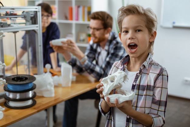 Niño emocionado en camisa a cuadros jugando con modelo de dinosaurios mientras inspira lección