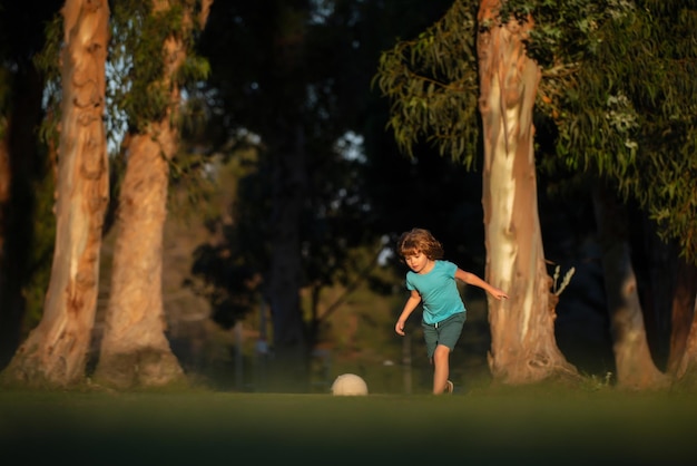 Niño emocionado niño pateando la pelota en el césped al aire libre fútbol niños jugar fútbol joven deportivo