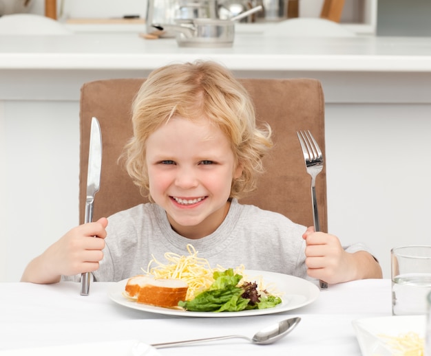 Niño emocionado con tenedores para comer pasta y ensalada