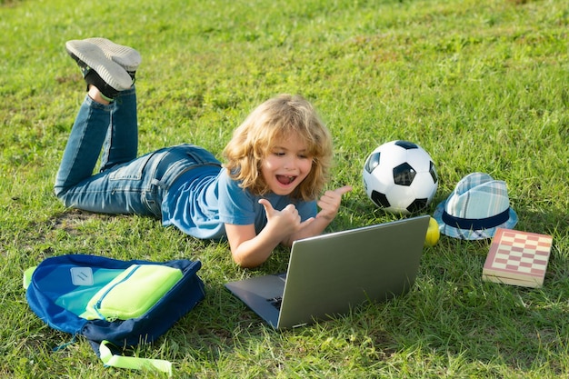 Niño emocionado usando una computadora portátil en el parque aprendiendo el concepto de educación al aire libre en línea