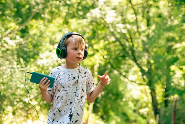 Niño emocional de 9 años en el bosque con auriculares escuchando música