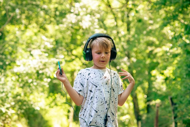 Niño emocional de 9 años en el bosque con auriculares escuchando música