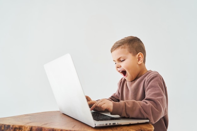 Niño emocional jugar juegos en línea en la computadora portátil adicción al juego chico guapo jugador está jugando en la computadora portátil sobre fondo blanco