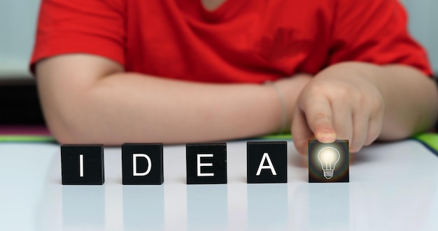 Niño empuje cubo de madera de bombilla de idea en la mesa