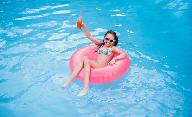 Niño encantado con bebida de frutas enfriándose en la piscina