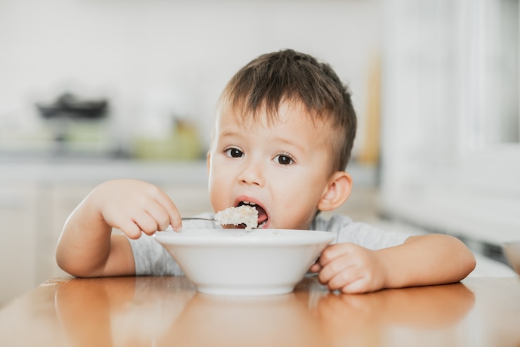 Foto un niño encantador con una camiseta en la cocina come avena con mucha avidez