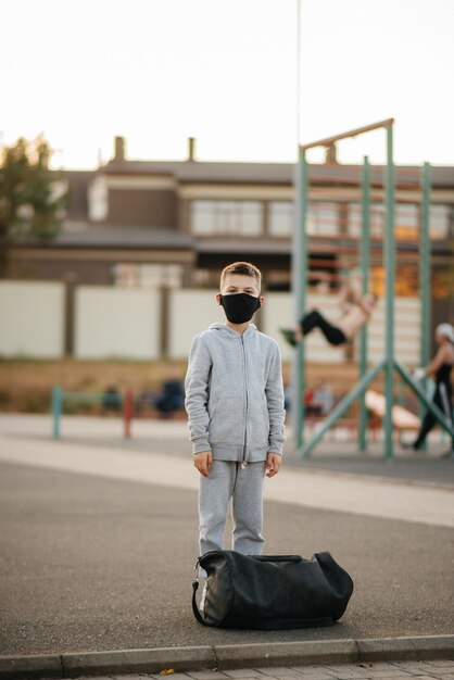 Un niño se encuentra en un campo de deportes después de un entrenamiento al aire libre durante la puesta de sol con una máscara