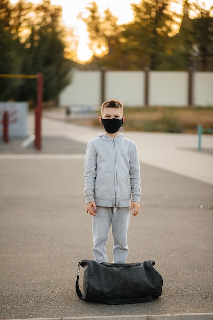 Un niño se encuentra en un campo de deportes después de un entrenamiento al aire libre durante la puesta de sol con una máscara