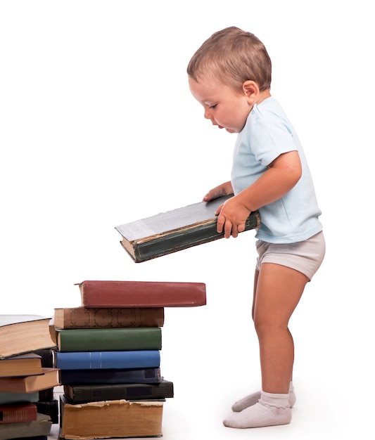 Niño se encuentra cerca de una pila de libros para un retrato educativo, aislado sobre una superficie blanca