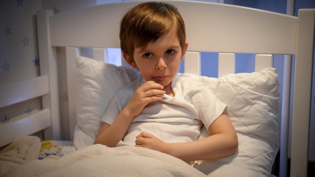 Foto un niño enfermo acostado en la cama y midiendo la temperatura corporal con un termómetro