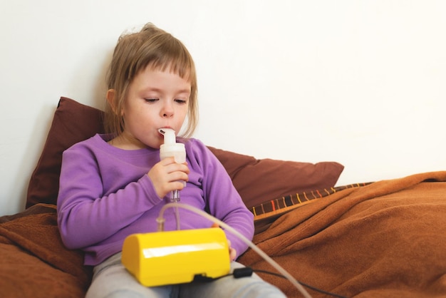 El niño enfermo se acuesta en la cama y hace inhalación usando un nebulizador tratamiento de la tos con inhalación