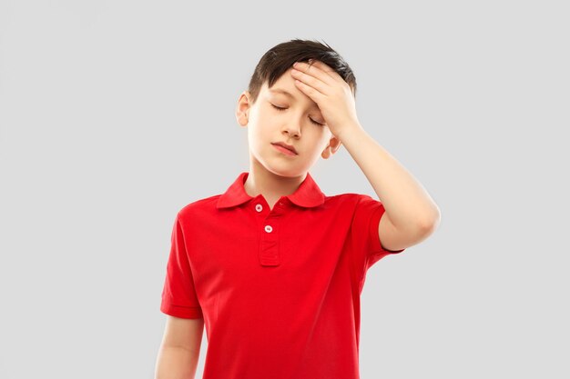 niño enfermo con camiseta roja sufriendo de dolor de cabeza