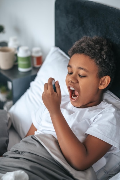 Niño enfermo con dolor de garganta y rociando el remedio