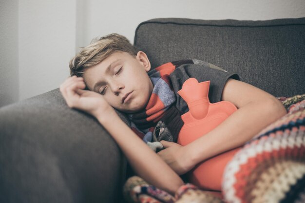 Foto niño enfermo durmiendo con una botella de agua caliente en el sofá