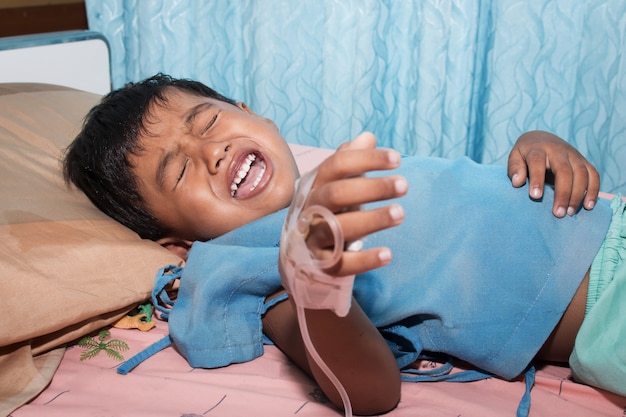 Niño enfermo y llorando en la cama del paciente