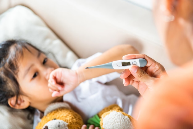 Niño enfermo Madre padre chequeando la temperatura de su hija enferma con termómetro digital en la boca niño acostado en la cama tomando la medición de su temperatura para la fiebre y la enfermedad atención médica