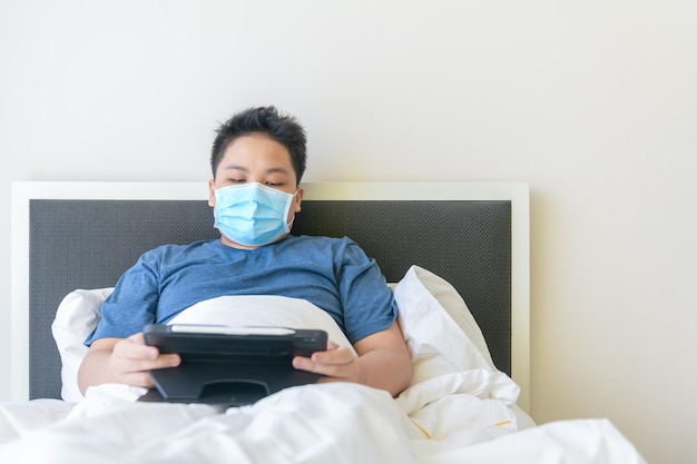 Niño enfermo con máscara y estudiando en línea con tableta pn cama nueva normalidad y educación