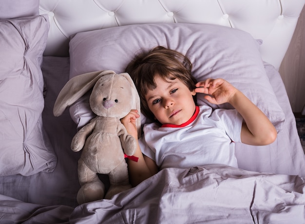 Foto un niño enfermo en pijama está acostado en la cama con un juguete suave