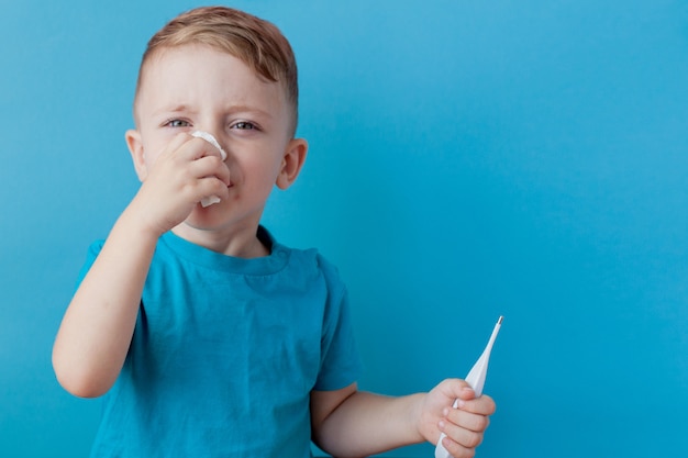 Niño enfermo con un termómetro, midiendo la altura de su fiebre y mirando a la cámara