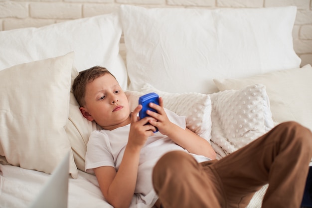 Niño enfocado está acostado en una cama y jugando un videojuego.