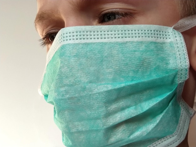 Niño enmascarado La cara de un niño de 7 años con una máscara quirúrgica protectora primer plano Colegial con cabello rubio y ojos gris azulado sobre fondo blanco