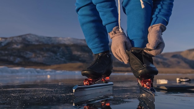 El niño entrena en patinaje de velocidad sobre hielo. El atleta se pone patines. La chica patina en invierno con ropa deportiva, gafas deportivas. Cámara lenta al aire libre.