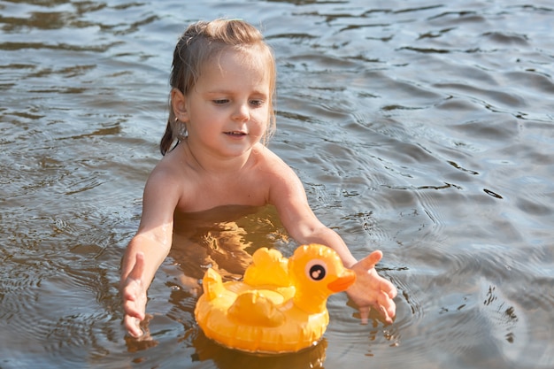 Niño entusiasta y enérgico que nada solo en el agua, disfruta del descanso en el río limpio, pasa las vacaciones de verano en unidad con la naturaleza, juega con su juguete, tiene un pato de goma en la superficie del agua.