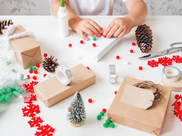 Foto niño envuelve regalos de navidad en papel de artesanía con decoraciones regalos para la celebración del año nuevo