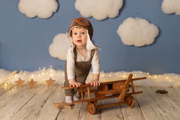 El niño es un niño con traje de piloto con un avión de madera sobre un fondo de nubes blancas