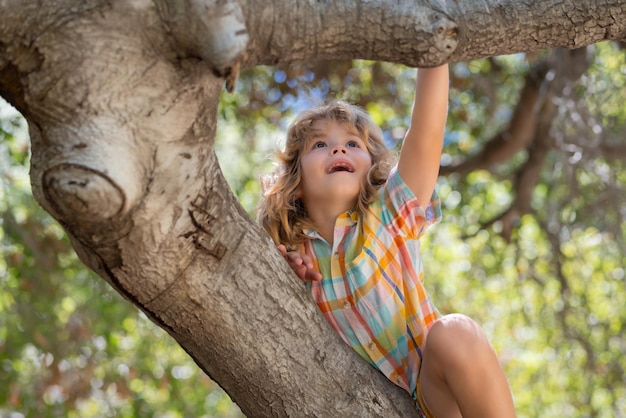 Niño escalando un árbol niño feliz jugar en el jardín de verano niño en un árbol con una rama grande