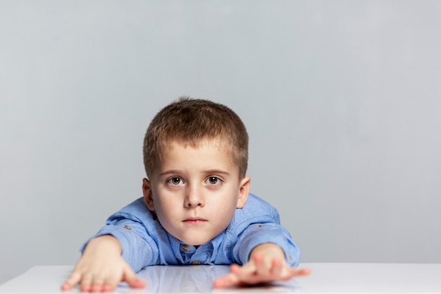 Un niño escolar cansado se sienta a la mesa con los brazos extendidos hacia adelante.