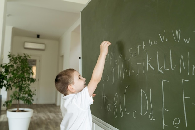 Niño escribiendo letras del abecedario en la pizarra verde