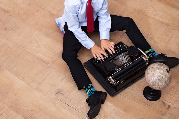 El niño está escribiendo en una vieja máquina de escribir. colegial con una máquina vintage. el niño se sienta en el suelo y sostiene una máquina de escribir retro. primer plano de la mano del niño como ejecutivo de negocios con máquina de escribir. colegio