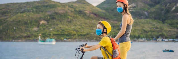 Niño de la escuela activa y su madre con máscara médica y casco de seguridad montando una bicicleta con mochila