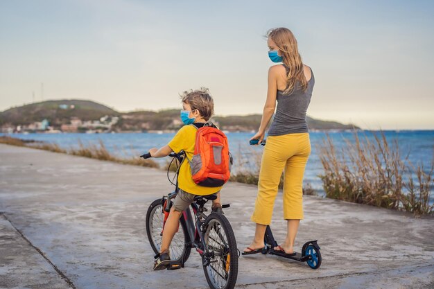 Niño de escuela activo y su madre con máscara médica montando en bicicleta con mochila en un día soleado Niño feliz en bicicleta de camino a la escuela Tienes que ir a la escuela con una máscara debido a la epidemia de coronavirus