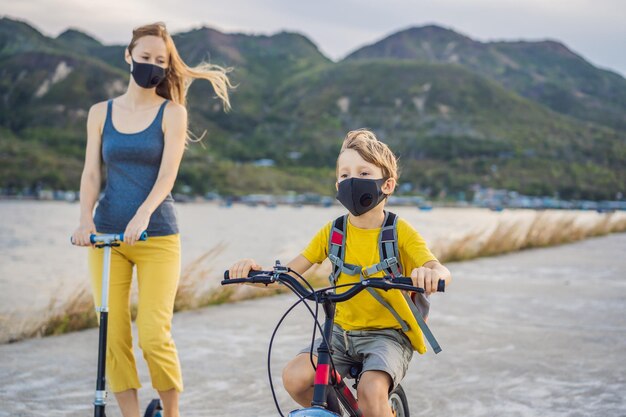 Niño de escuela activo y su madre con máscara médica montando en bicicleta con mochila en un día soleado Niño feliz en bicicleta de camino a la escuela Tienes que ir a la escuela con una máscara debido a la epidemia de coronavirus