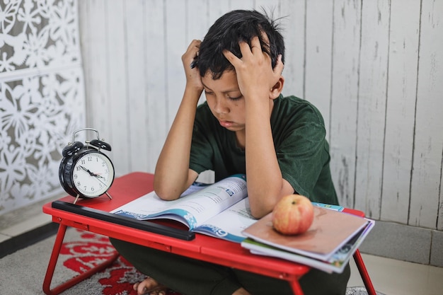 Niño de escuela agotado cansado de estudiar sosteniendo la cabeza con las manos sentado en el escritorio con papel