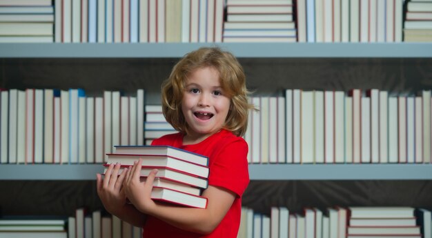 Niño de la escuela asombrado sostiene una pila de libros alumno del día del conocimiento con una pila de libros niños disfrutando del libro