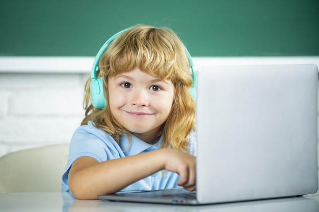 Niño de escuela divertida con auriculares y computadora portátil en clase en la escuela