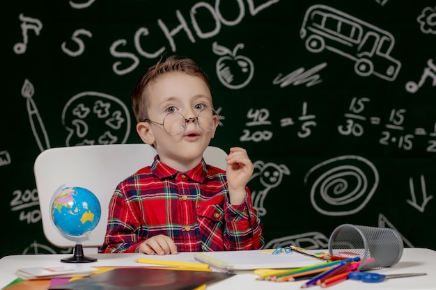 Niño de la escuela emocional sentado en el escritorio con muchos útiles escolares. Primer dia de escuela. Kid boy de la escuela primaria. De vuelta a la escuela. Niño de primaria.