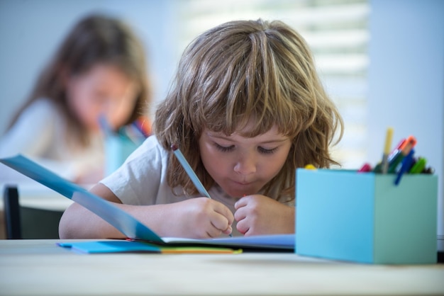 Niño de la escuela escribiendo algo en el cuaderno y sentado en la mesa en el aula de regreso a la escuela feliz smil