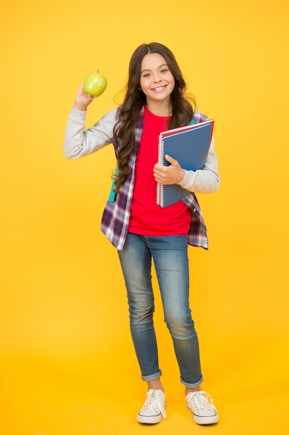 Niño de la escuela feliz sostener libros y manzana natural fruta fondo amarillo salud dental