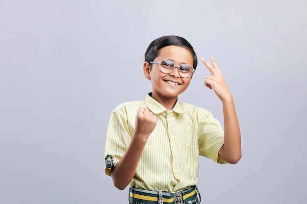 Niño de la escuela india dando gesto ganador sobre fondo blanco.