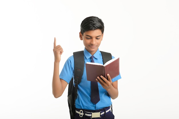 Niño de la escuela india en uniforme y diario de lectura sobre fondo blanco.