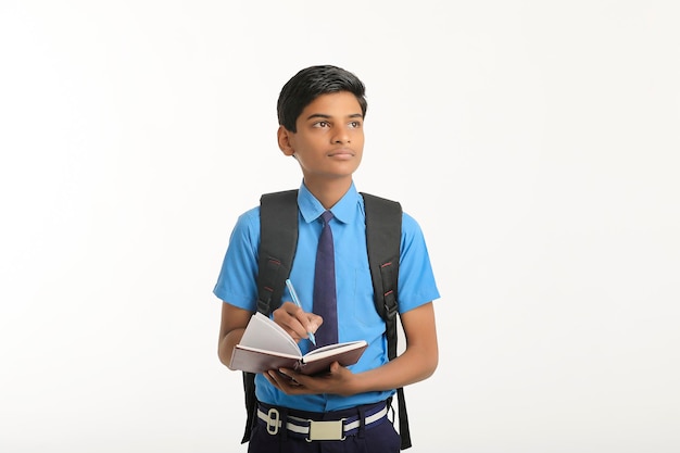 Niño de la escuela india en uniforme y sosteniendo el diario en la mano sobre fondo blanco.