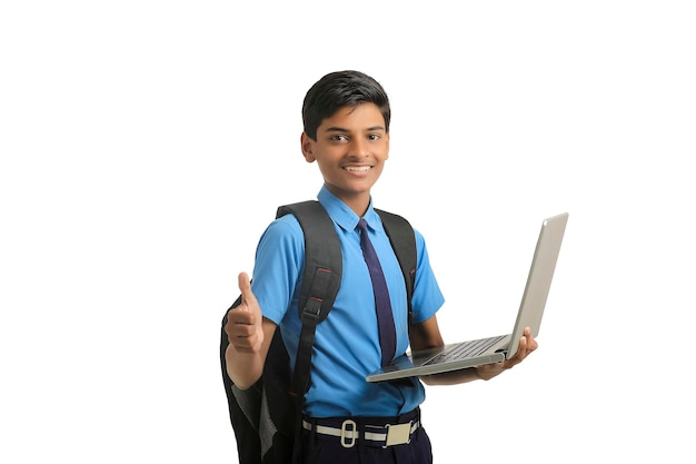 Niño de la escuela india en uniforme y usando una computadora portátil sobre fondo blanco.