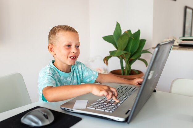 Niño de escuela joven que trabaja en casa con una computadora portátil y notas de clase que estudian en una clase virtual.