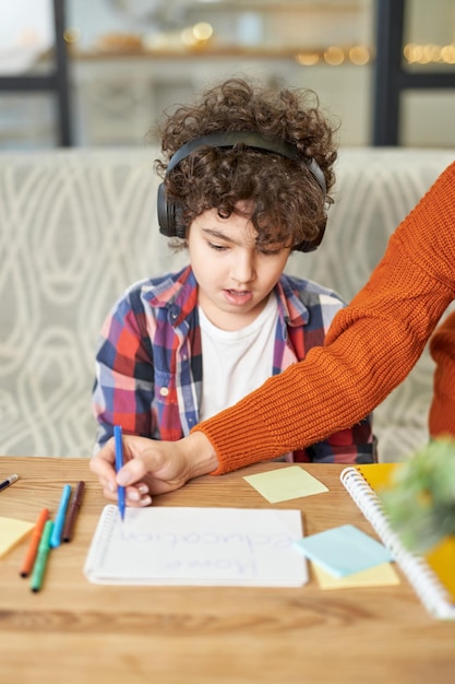 Niño de escuela latinoamericana con audífonos mirando sorprendido mientras su mamá lo ayuda a dibujar