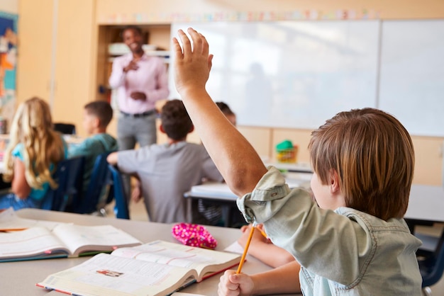 Niño de escuela levantando la mano para responder una pregunta en una clase escolar